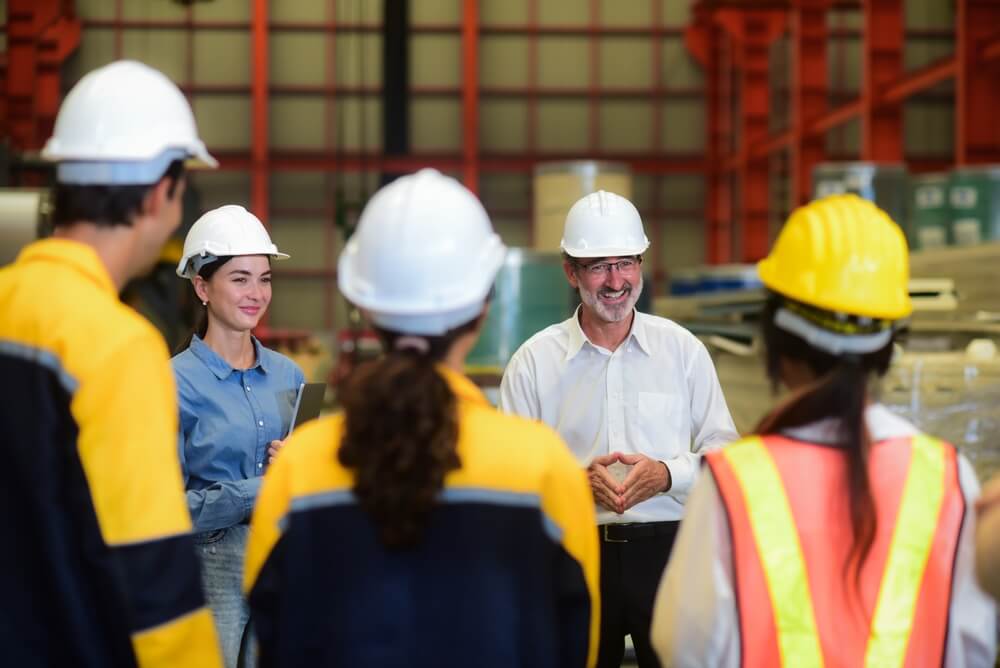 Group of manufacturers in a factory meeting with boss discussing work for the day.